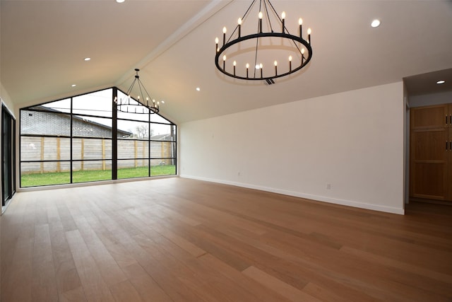 interior space with vaulted ceiling, a notable chandelier, wood finished floors, and baseboards