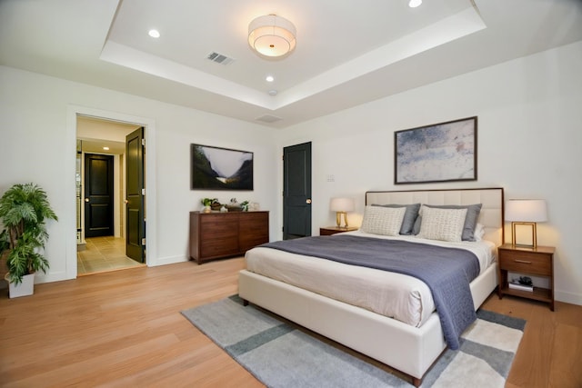 bedroom with visible vents, light wood-style flooring, a tray ceiling, recessed lighting, and baseboards