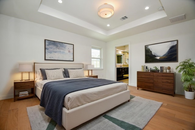 bedroom with a tray ceiling, recessed lighting, light wood-style floors, and visible vents