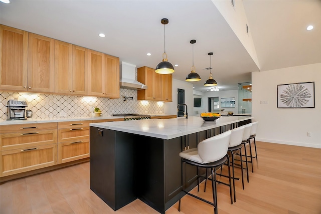 kitchen with light wood-type flooring, a large island, wall chimney range hood, decorative backsplash, and range