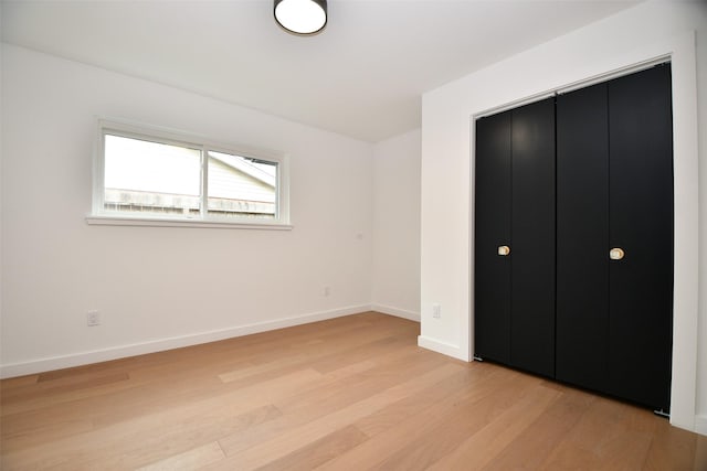 unfurnished bedroom featuring light wood-style flooring, baseboards, and a closet