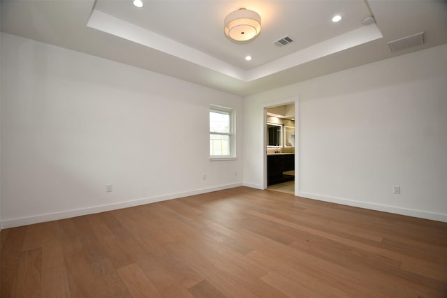 unfurnished room with visible vents, recessed lighting, baseboards, light wood-style floors, and a raised ceiling