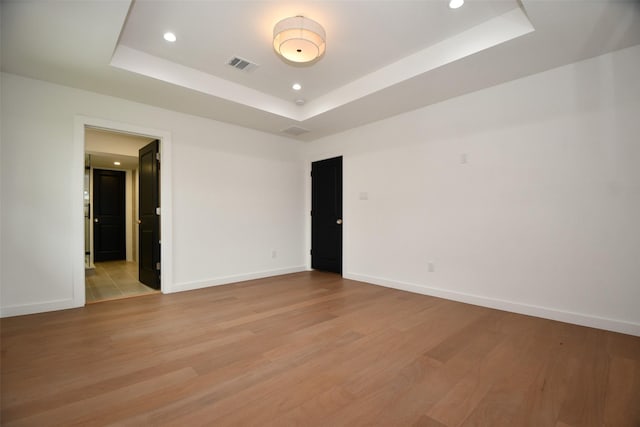 spare room with visible vents, a raised ceiling, baseboards, and light wood-style flooring