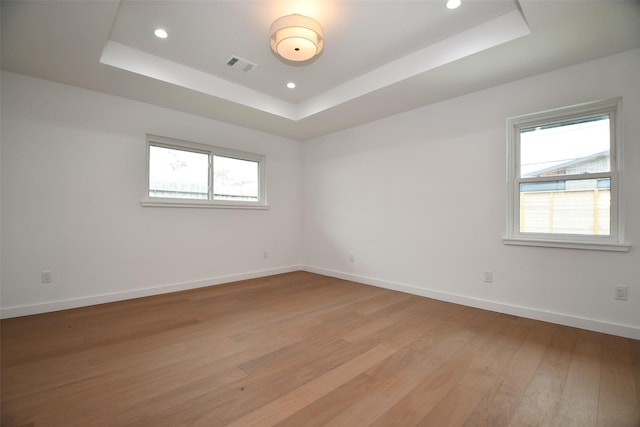 empty room featuring visible vents, a raised ceiling, light wood-style floors, and baseboards