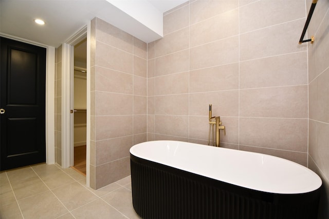 full bathroom featuring tile patterned flooring, tile walls, a freestanding tub, and a walk in closet