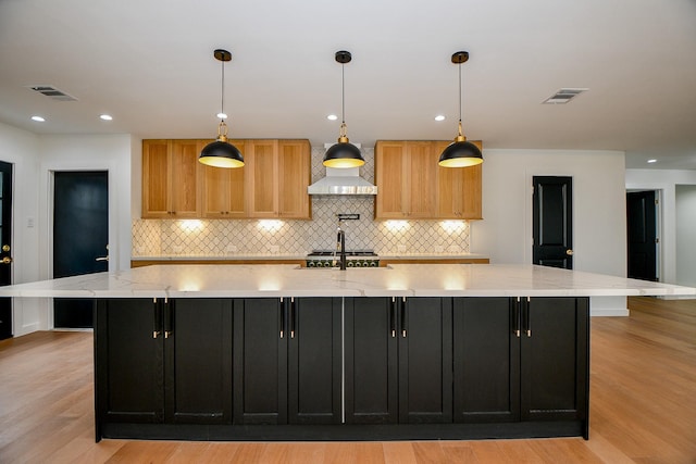 kitchen with light wood-style flooring, range, visible vents, and a large island with sink