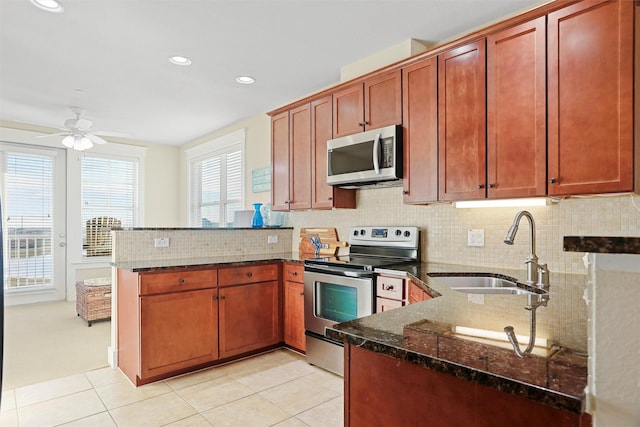 kitchen with a sink, stainless steel appliances, dark stone counters, a peninsula, and decorative backsplash