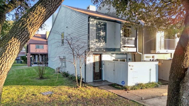 rear view of house featuring a balcony, a gate, a yard, and fence