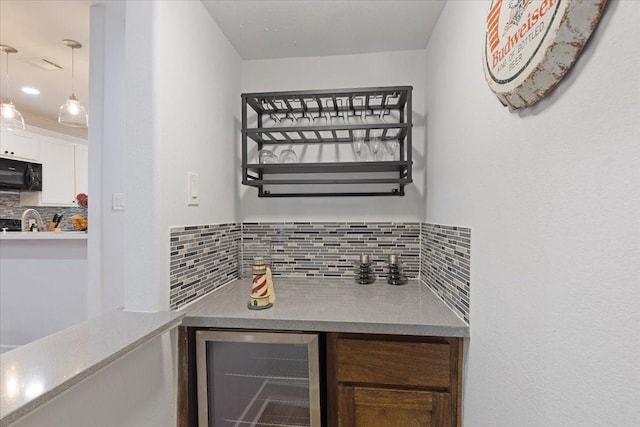 bar with beverage cooler, backsplash, black microwave, a dry bar, and hanging light fixtures