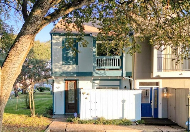 exterior space featuring a balcony, a lawn, a fenced front yard, and stucco siding