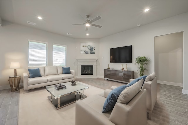 living room featuring a glass covered fireplace, recessed lighting, baseboards, and wood finished floors