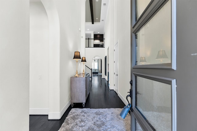 corridor with arched walkways, baseboards, a towering ceiling, and dark wood-style flooring