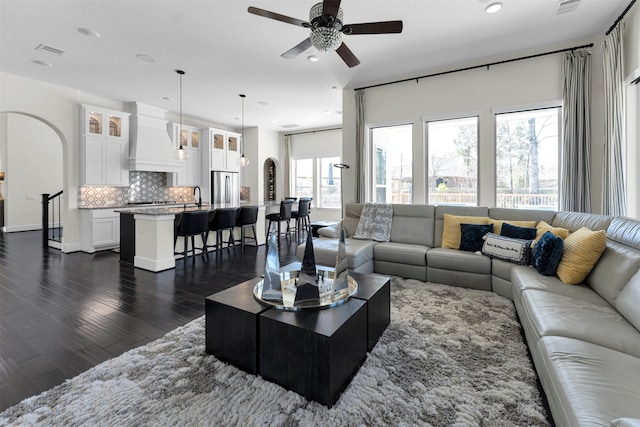 living area featuring visible vents, a ceiling fan, dark wood finished floors, recessed lighting, and arched walkways