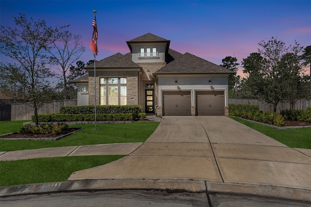 prairie-style home with stucco siding, driveway, stone siding, fence, and an attached garage