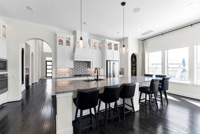 kitchen featuring visible vents, a sink, stainless steel appliances, arched walkways, and decorative backsplash