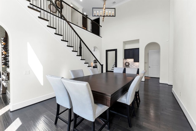 dining space with arched walkways, dark wood finished floors, stairs, and baseboards