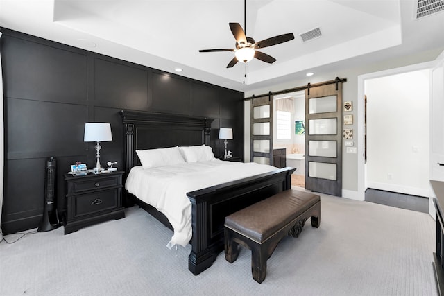 bedroom with a tray ceiling, a decorative wall, a barn door, and visible vents