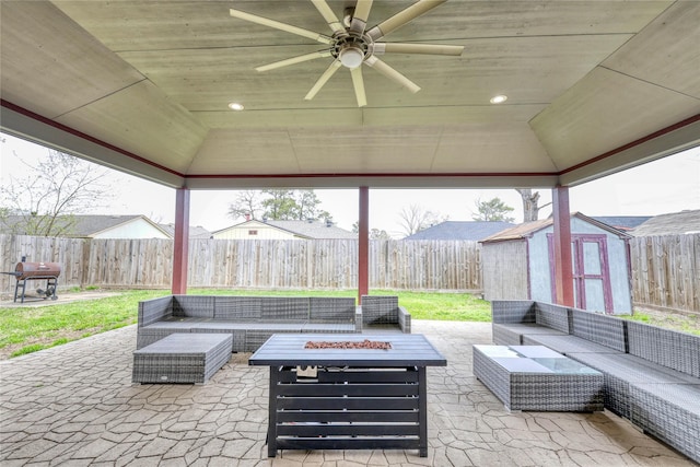 view of patio featuring an outdoor living space with a fire pit, a fenced backyard, an outbuilding, a storage unit, and a ceiling fan