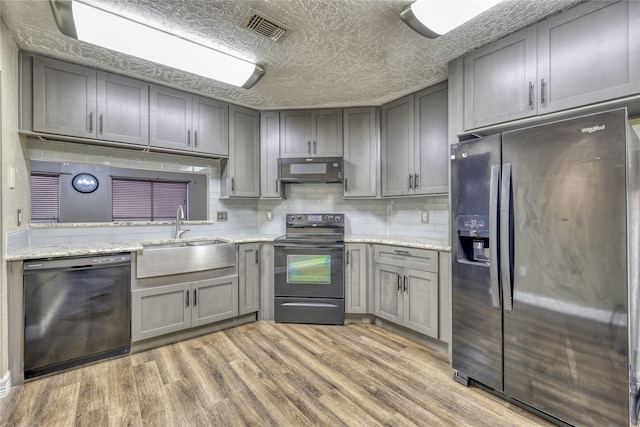 kitchen featuring visible vents, light wood finished floors, gray cabinets, a sink, and black appliances