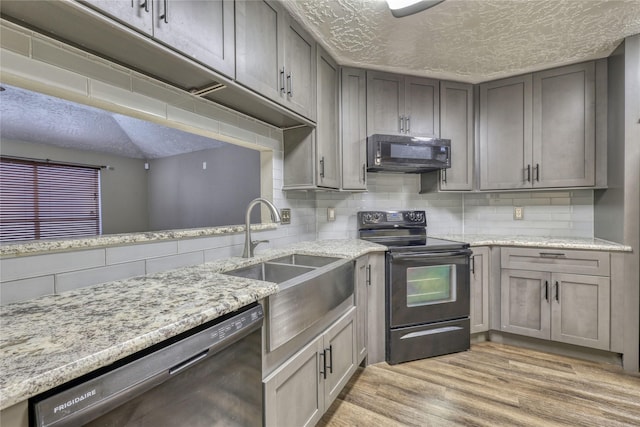 kitchen featuring black appliances, light wood finished floors, backsplash, and a sink