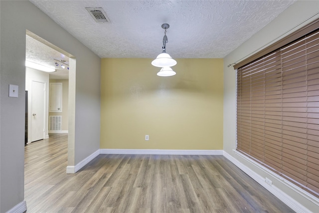 unfurnished dining area featuring visible vents, a textured ceiling, baseboards, and wood finished floors