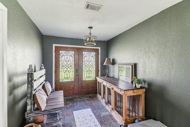 entrance foyer featuring stone tile flooring, visible vents, a chandelier, and a textured wall