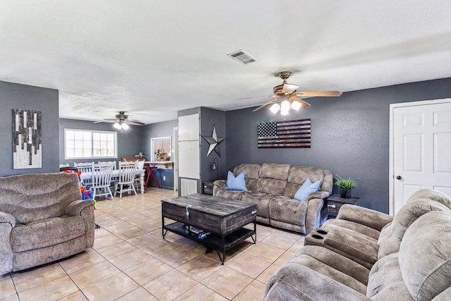 living area with light tile patterned floors, visible vents, a ceiling fan, and a textured wall