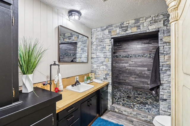 full bathroom with toilet, vanity, tiled shower, wood finished floors, and a textured ceiling