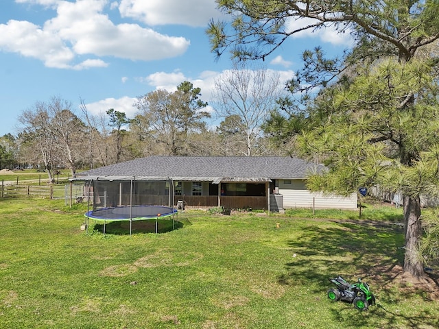 rear view of house featuring a lawn, a trampoline, and fence