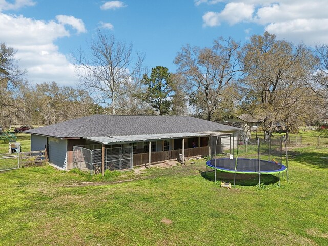 rear view of property with an outdoor structure, a trampoline, and a shingled roof