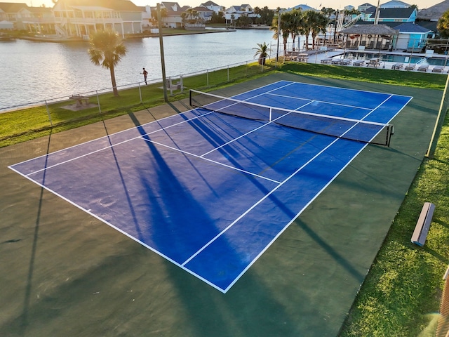 view of sport court with a residential view, a water view, and fence