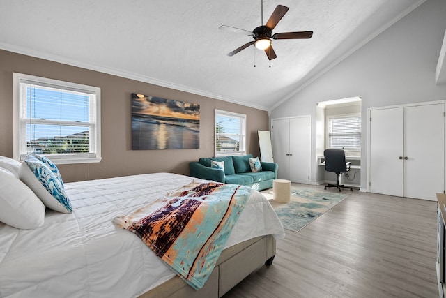 bedroom featuring two closets, ornamental molding, a textured ceiling, wood finished floors, and lofted ceiling