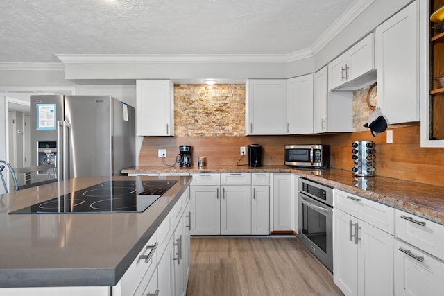 kitchen featuring light wood finished floors, white cabinets, appliances with stainless steel finishes, crown molding, and tasteful backsplash