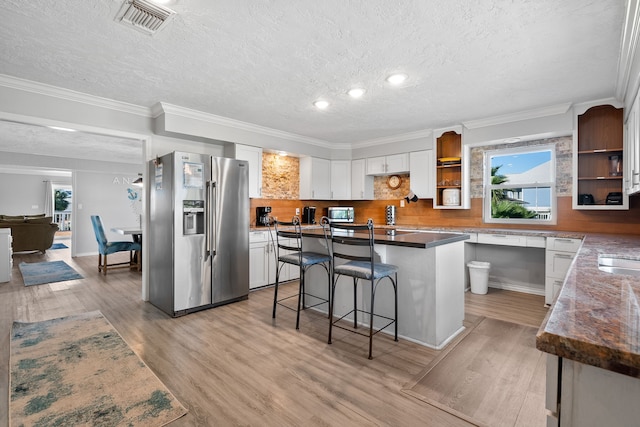 kitchen featuring stainless steel fridge with ice dispenser, light wood-type flooring, a kitchen breakfast bar, white cabinets, and open shelves