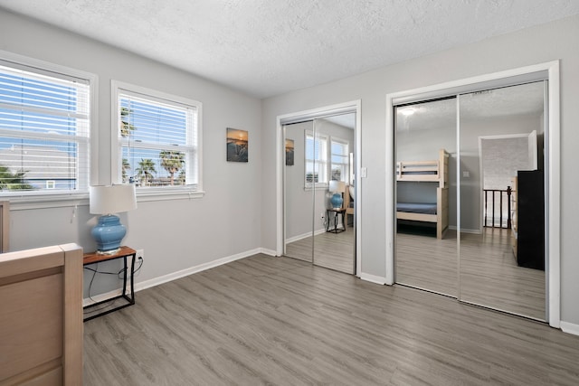 bedroom featuring multiple windows, a textured ceiling, two closets, and wood finished floors