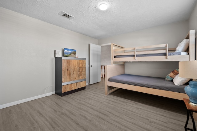 bedroom featuring visible vents, baseboards, a textured ceiling, and wood finished floors