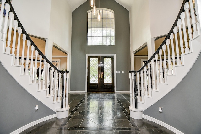 foyer featuring french doors, baseboards, stone tile floors, and a towering ceiling