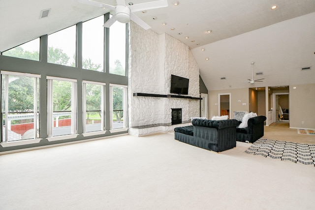 living room with a ceiling fan, visible vents, high vaulted ceiling, a stone fireplace, and light carpet