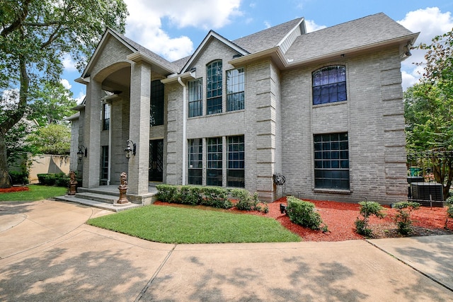 view of front of property with a front yard, brick siding, central AC, and a shingled roof