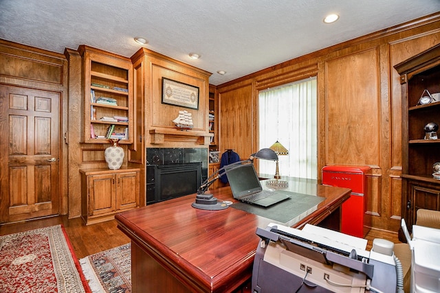 office area with built in features, a textured ceiling, wood finished floors, wood walls, and a fireplace