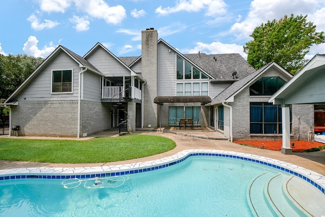 back of house featuring brick siding, a patio area, an outdoor pool, and a chimney