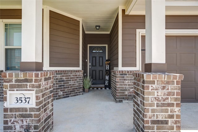 view of exterior entry featuring a garage, brick siding, and a porch