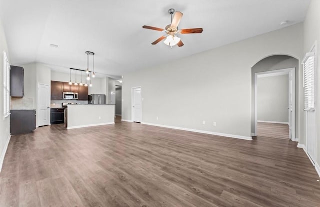 unfurnished living room with dark wood-type flooring, lofted ceiling, arched walkways, baseboards, and ceiling fan