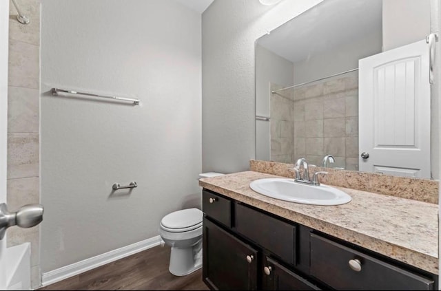 bathroom with baseboards, toilet, wood finished floors, vanity, and a shower