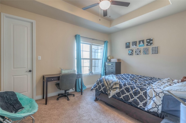 carpeted bedroom with a raised ceiling, baseboards, and ceiling fan