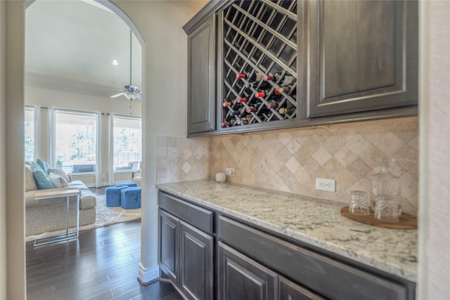 kitchen featuring tasteful backsplash, ceiling fan, light stone counters, arched walkways, and dark wood-style flooring