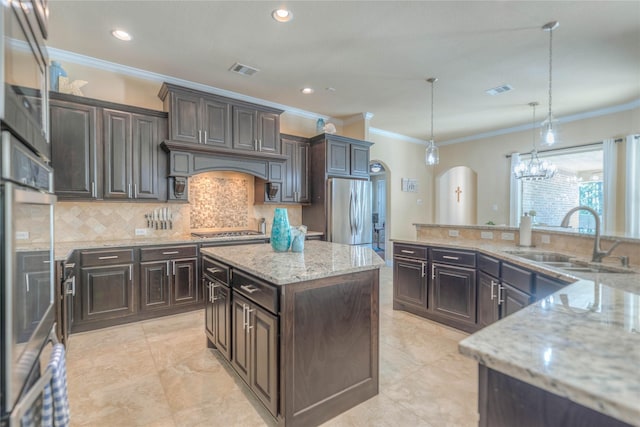 kitchen featuring visible vents, a kitchen island, arched walkways, a sink, and stainless steel appliances