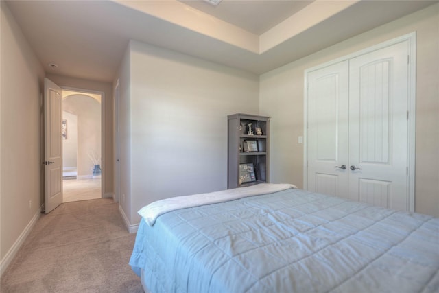 bedroom with baseboards, arched walkways, a closet, and light carpet