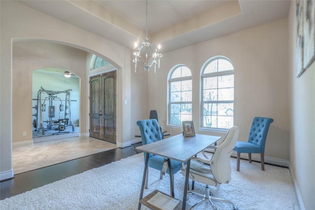 home office with a raised ceiling, wood finished floors, arched walkways, and baseboards