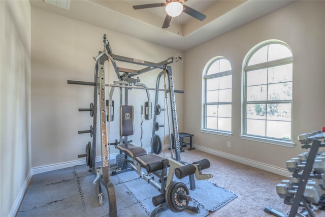 exercise area with baseboards, a raised ceiling, carpet floors, and ceiling fan